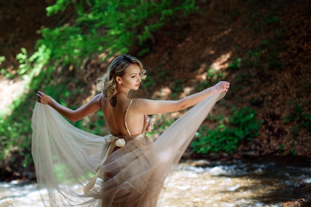 Piękna dziewczyna w sukience stoi w pobliżu koryta rzeki w naturze na zewnątrz