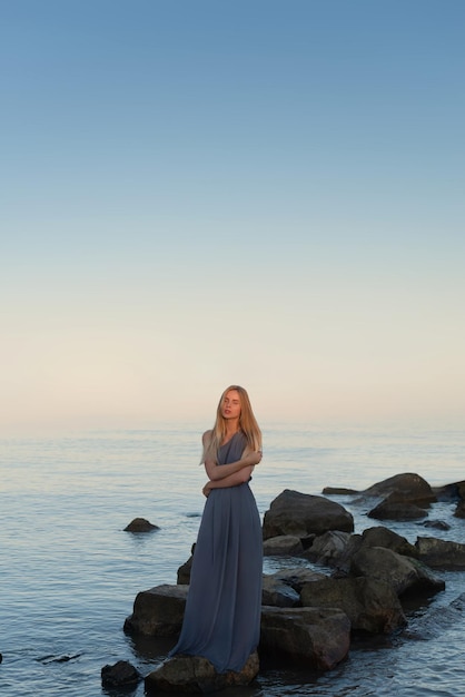 piękna dziewczyna w szarej sukience nad morzem o zachodzie słońca