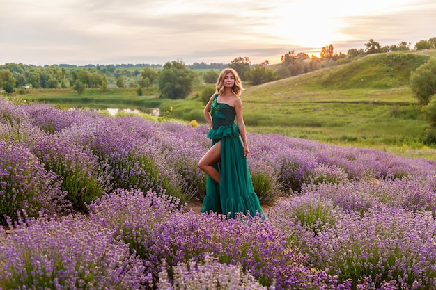 Piękna dziewczyna w zielonej sukience pozuje na lawendowym polu