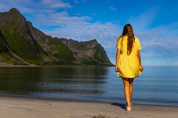 piękna dziewczyna w żółtej sukience spaceruje po plaży otoczonej potężnymi górami, senja, norwegia