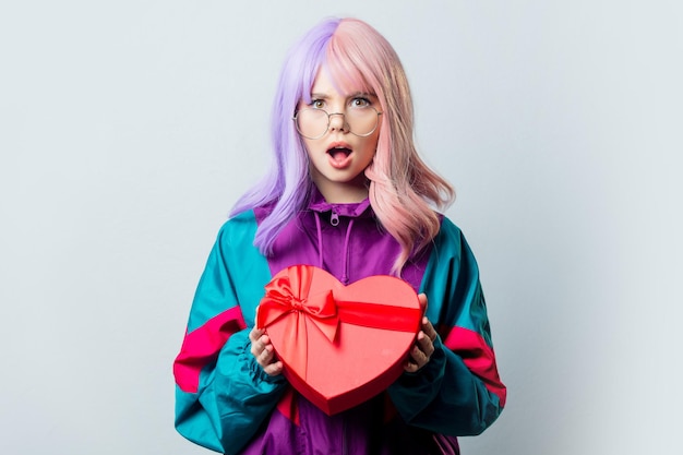 Piękna dziewczyna Yandere z fioletowymi włosami i dresem z lat 80. trzyma pudełko w kształcie serca na szarym tle