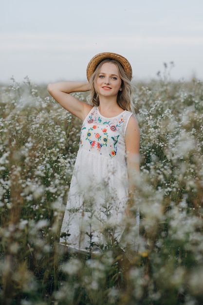 Piękna dziewczyna z czapką w ręku idzie w polu z kwiatami pola i uśmiecha się