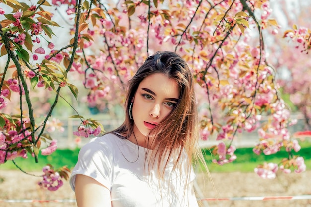 Piękna dziewczyna z długimi włosami cieszy się pięknem wiosennej przyrody w pobliżu kwitnącej sakury.
