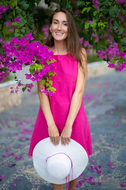 Piękna dziewczyna z kapeluszem w dłoniach stoi w pobliżu kwitnącego drzewa z różowymi kwiatami