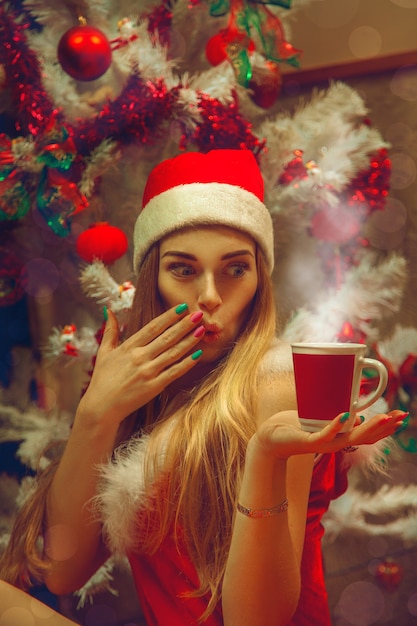 Piękna dziewczyna z piegami przy filiżance gorącej herbaty w pobliżu choinki. Świąteczny nastrój. Nowy Rok.