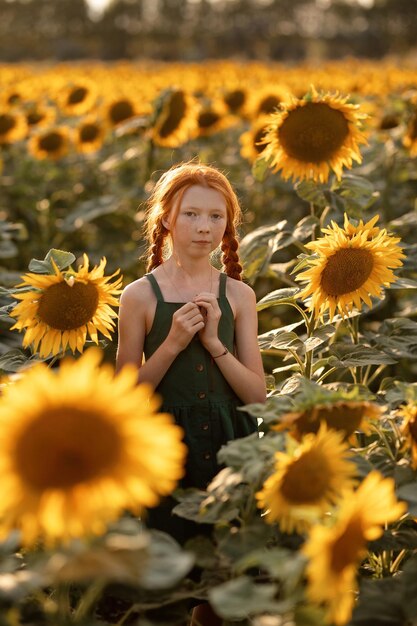 Piękna dziewczyna z rudymi włosami i piegami stoi na polu ze słonecznikami