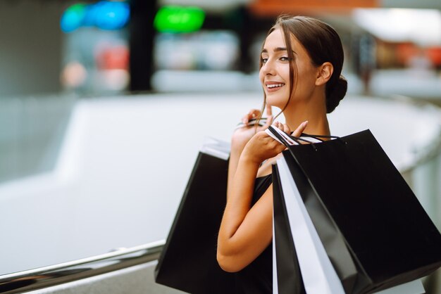 Piękna dziewczyna z torby na zakupy patrząc na kamery i uśmiechając się robiąc zakupy w centrum handlowym