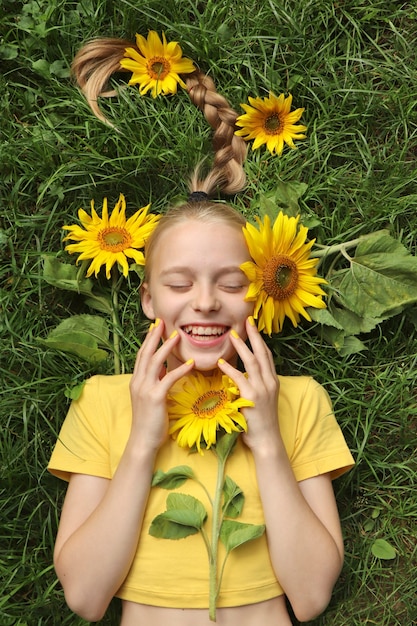 Zdjęcie piękna dziewczyna z żółtym manicure leży na trawie z słonecznikami