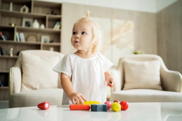 Piękna dziewczynka bawi się sama w domu z kolorowymi drewnianymi zabawkami swoich dzieci