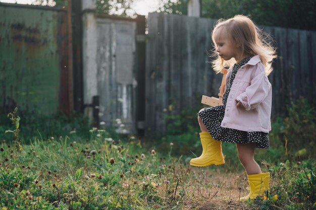 Zdjęcie piękna dziewczynka w sukience idzie z samolotem w rękach przez polanę szczęśliwe wolne dzieciństwo na wsi dziecko bawi się samolotem marzy o zostaniu pilotem