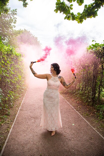 Piękna elegancka brunetka kobieta w różowej sukience z kolorowym dymem