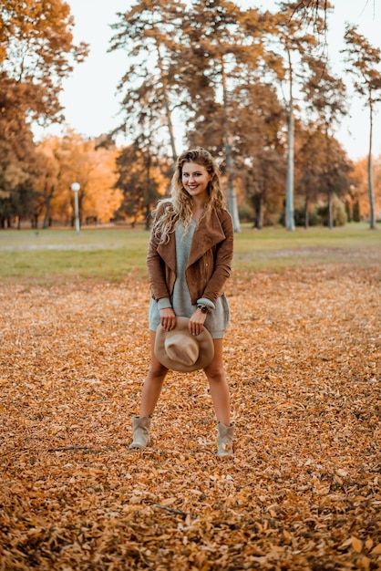 Piękna elegancka kobieta stoi w parku w jesieni i trzyma kapelusz.