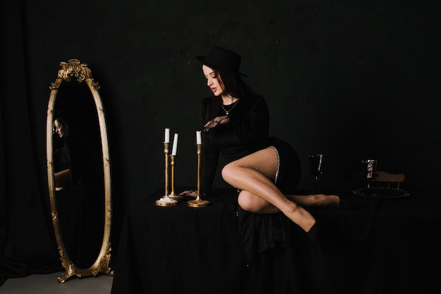 Piękna elegancka kobieta w rękawiczkach i sukience siedzi na stole na czarnym tle