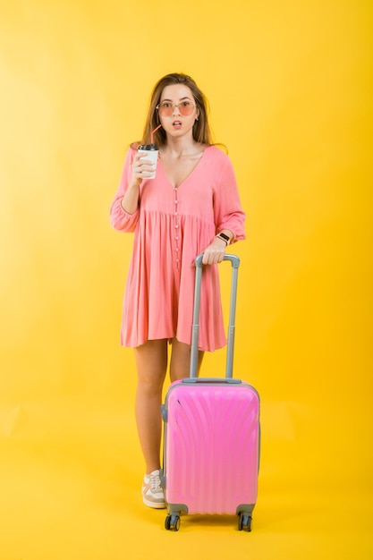 Piękna elegancka kobieta w różowej sukience z różową dużą walizką do podróży