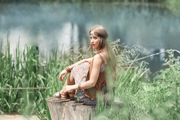 Piękna hipis dziewczyna siedzi na pniu i patrząc na staw. pojęcie jedności z naturą