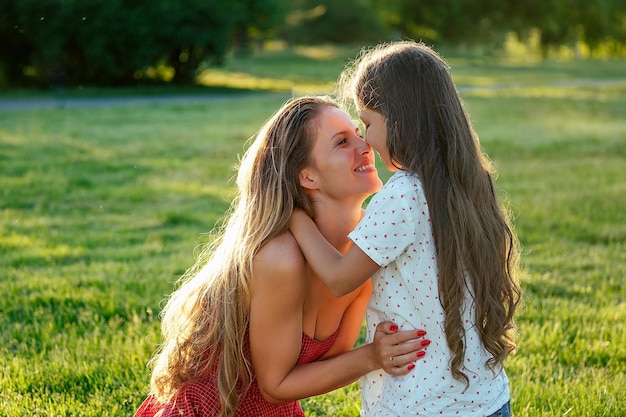 Piękna i młoda długowłosa kobieta bawi się z córką w objęciach i pieszczotach w letni dzień w parku. szczęśliwe macierzyństwo i cudowna koncepcja dzieciństwa