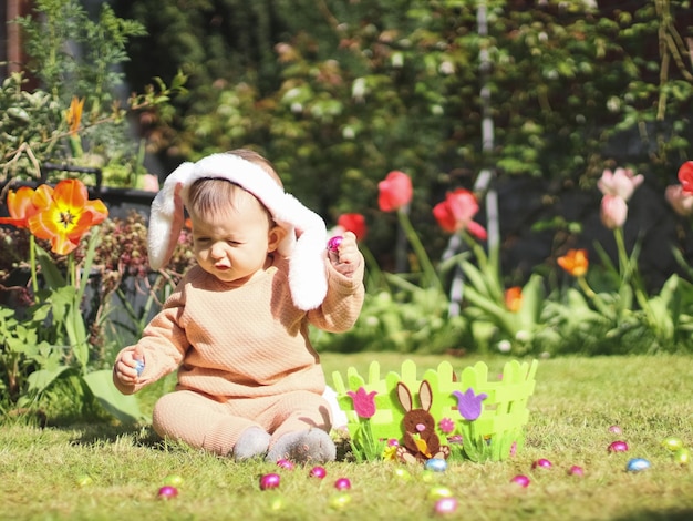 Piękna i urocza kaukaska dziewczynka z uszami królika z pałąkiem na głowę siedzi na trawniku z kwiatami