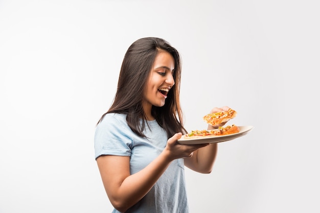 Piękna indyjska azjatycka młoda dziewczyna je kawałek pizzy stojąca na białym tle na białym tle