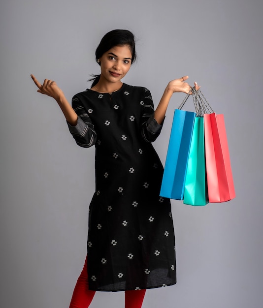Piękna indyjska młoda dziewczyna trzyma i pozuje z torby na zakupy na szaro
