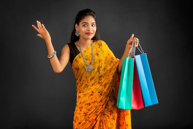 Piękna indyjska młoda dziewczyna trzyma i pozuje z torby na zakupy na szarym tle