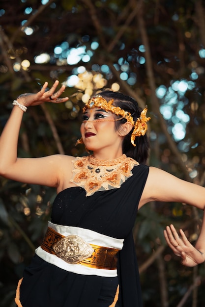 Piękna jawajska kobieta pozuje z ręką w czarnym kostiumie, mając na sobie złotą koronę i złoty naszyjnik