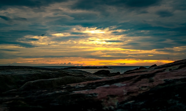 Piękna kamień plaża w ranku z złotym wschodu słońca niebem. Cicha i spokojna scena. Krajobraz spokojnego morza rano. Seascape z panoramą. Morze tropikalne.