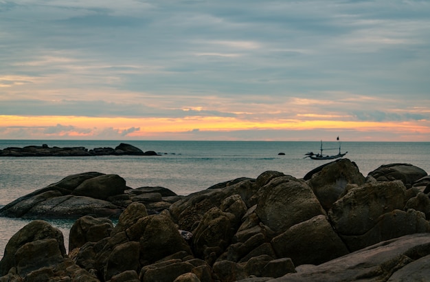 Piękna kamień plaża w ranku z złotym wschodu słońca niebem. Rybak w długi ogon łodzi z kultury ludowej połowów. Cicha i spokojna scena. Rano spokojne morze.