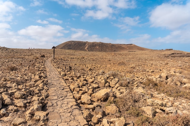 Piękna kamienna ścieżka do krateru wulkanu Calderon Hondo w pobliżu Corralejo, północne wybrzeże wyspy Fuerteventura, Wyspy Kanaryjskie. Hiszpania