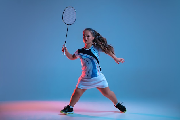 Piękna karłowata kobieta ćwicząca w badmintonie na niebieskim tle w świetle neonowym