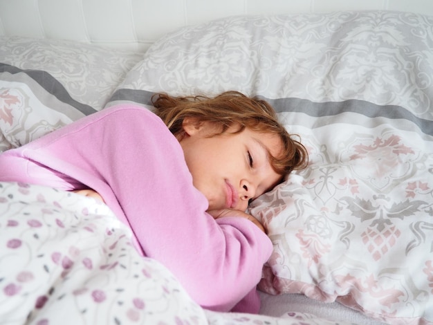 Piękna kaukaska dziewczyna o blond włosach, ubrana w różową piżamę, śpi na łóżku