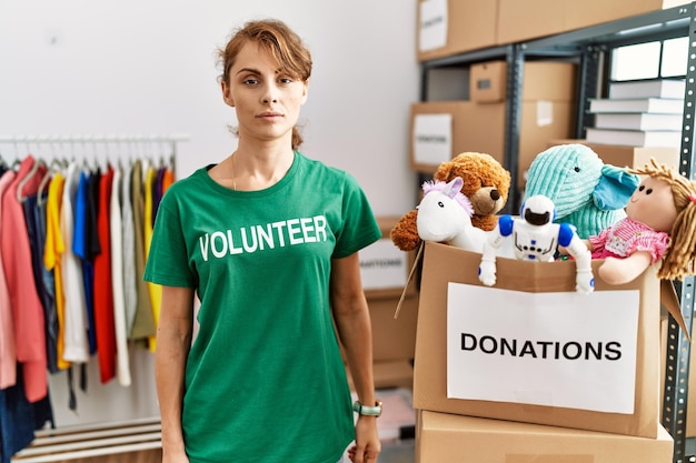 Piękna kaukaska kobieta ubrana w koszulkę wolontariusza przy darowiznach stoi zrelaksowana z poważnym wyrazem twarzy. proste i naturalne patrzenie w kamerę.
