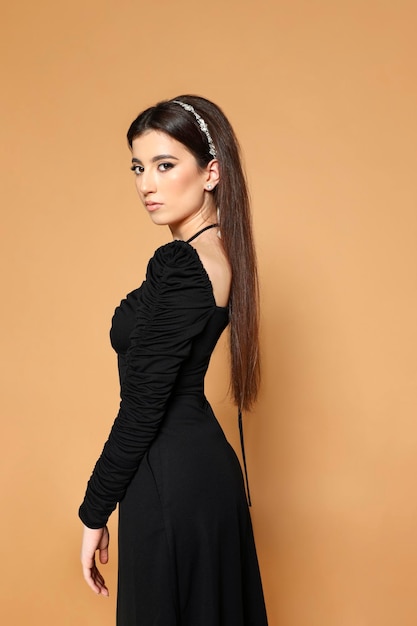 Piękna kaukaska młoda kobieta z prostymi włosami w czarnej sukience pozuje w profilu na białym tle beżowym