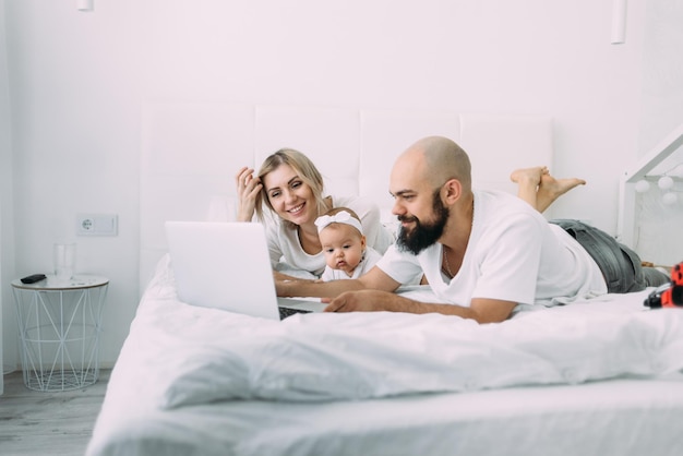 Piękna kaukaska rodzinna mama córka i brodaty tata leżą rano na łóżku w sypialni i oglądają bajki na laptopie Rodzice i dzieci