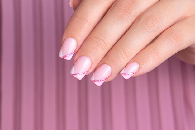 Piękna kobieca dłoń z różowymi i białymi paznokciami do manicure, błyszczącymi francuskimi wzorami