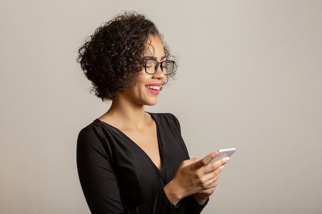 Piękna Kobieta Afro Uśmiecha Się, W Okularach I Przy Użyciu Smartfona