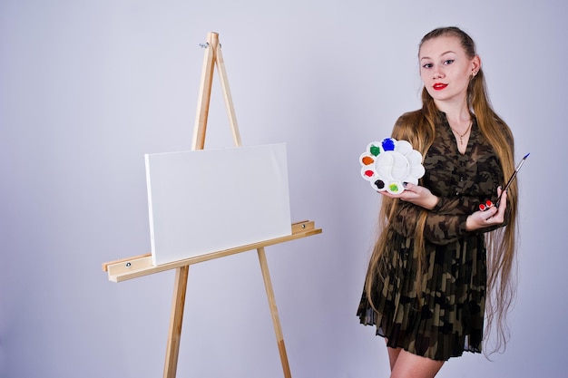 Piękna kobieta artysta malarz z pędzlami i płótnem olejnym pozuje w studio na białym tle