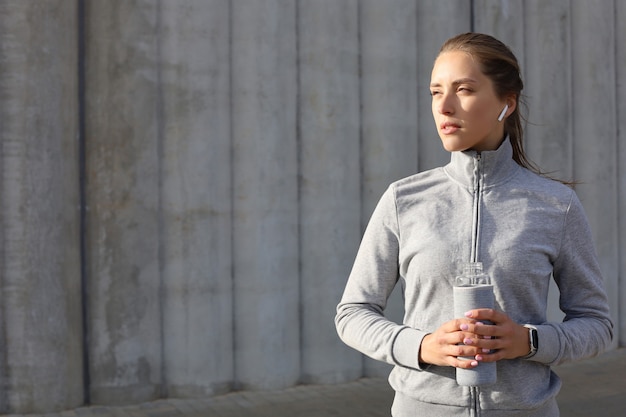 Piękna kobieta biegacz stoi na zewnątrz trzymając butelkę wody. Fitness kobieta robi sobie przerwę po uruchomieniu treningu.