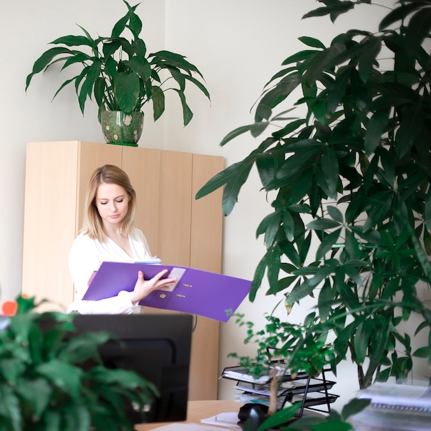Zdjęcie piękna kobieta biznesowa trzyma fioletowy folder dokumentów w nowoczesnym biurze na tle roślin