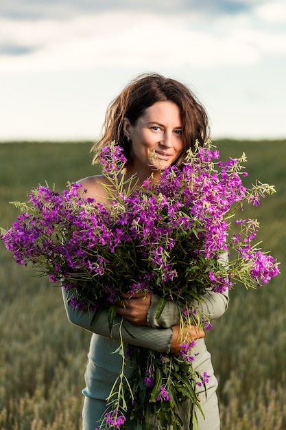 piękna kobieta, ciesząc się aromatem bukiet kwiatów łubinu fioletowego w kwiatowym polu