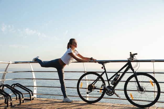 Piękna kobieta fitness robi ćwiczenia rozciągające na plaży, jazda na rowerze