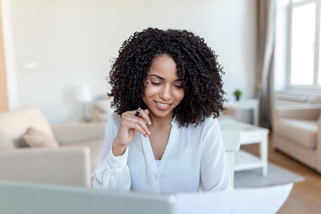 Piękna kobieta freelancer notująca informacje dotyczące planowania projektu wykonującego zdalną pracę za pomocą laptopa Kobieta śmiejąca się podczas czytania wiadomości e-mail na nowoczesnym urządzeniu przenośnym