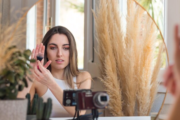 Zdjęcie piękna kobieta influencer vloguje w aparacie pokazując jej ulubiony pędzel do mekupu