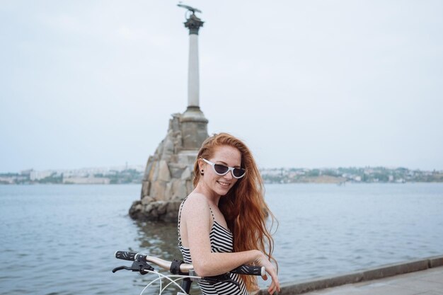 Piękna kobieta jedzie na rowerze Styl życia i zdrowie w mieście Wesoła rudowłosa młoda kobieta czerpie przyjemność z chodzenia po mieście