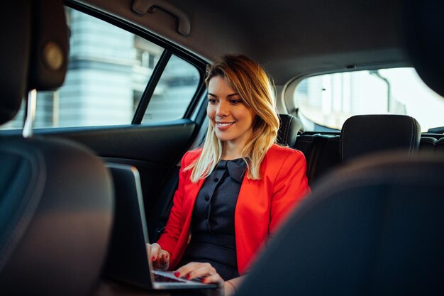 Piękna kobieta korzysta z laptopa siedząc na tylnym siedzeniu samochodu