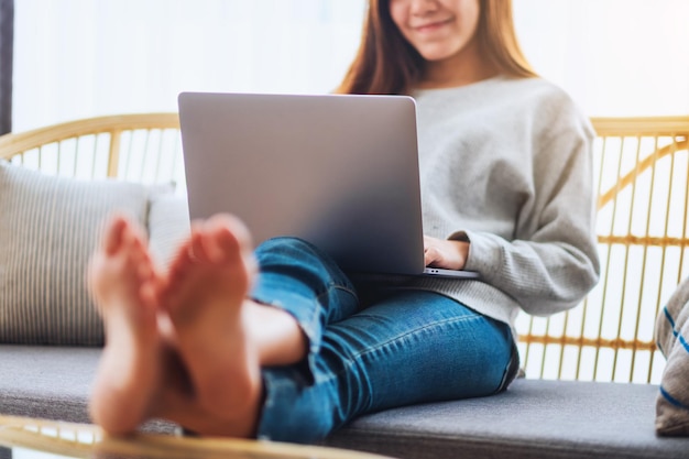 Piękna kobieta korzystająca z laptopa i pracująca na nim, leżąc na kanapie w domu