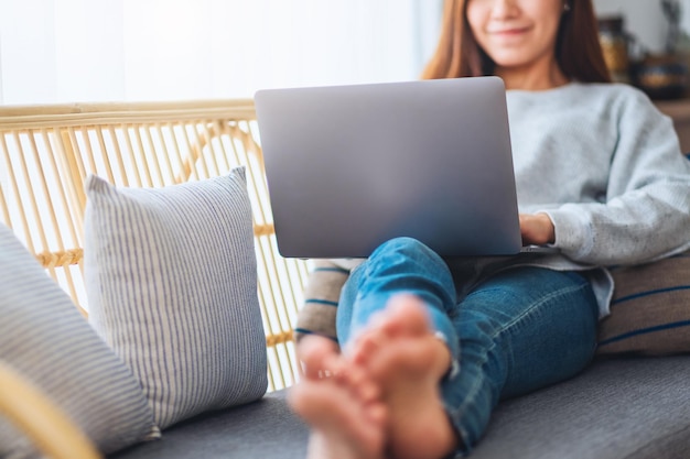 Piękna kobieta korzystająca z laptopa i pracująca na nim, leżąc na kanapie w domu