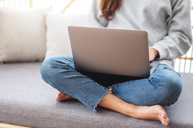 Piękna kobieta korzystająca z laptopa i pracująca na nim, siedząc na kanapie w domu