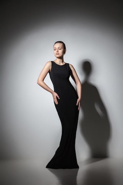 Piękna kobieta model pozuje w eleganckiej czarnej sukience w studio