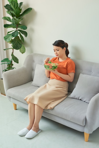 Piękna kobieta na kanapie je zdrową sałatkę