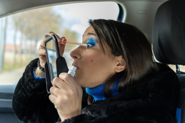Piękna kobieta nakłada makijaż oczu w samochodzie z lustrem